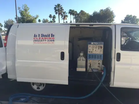 A white van with the As It Should Be Cleaning sign on its side, the side door open on a carpet cleaning machine with hoses running out