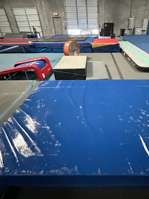 Blue gym mats wet and streaked from wiping, with sprung floors and gym equipment behind